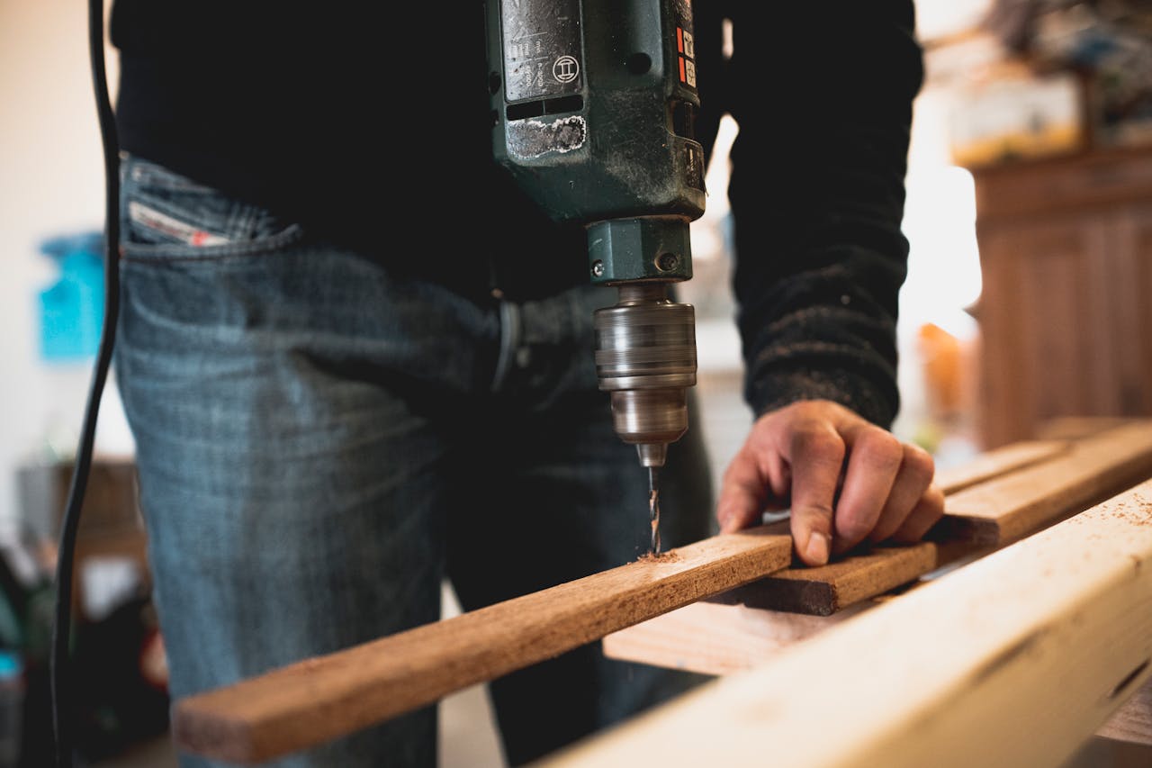 Home Close-up of a person using an electric drill on a wooden plank, showcasing detailed woodworking skills.